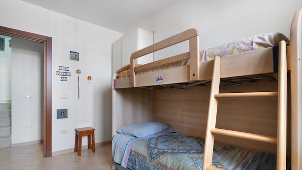 Ein Zimmer mit einem Etagenbett, einem kleinen Holzhocker und einem an der Wand befestigten Lichtschalter.