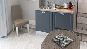 A compact kitchen with grey cabinets, a microwave, a sink, and a small dining table with a remote control. - Apartment 'Fede's Home' with Private Terrace, Wi-Fi and Air Conditioning (Fiumicino)