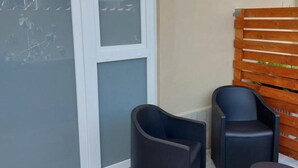 A balcony with a sliding glass door, two black chairs, a small round table, and a wooden slatted wall. - Apartment 'Fede's Home' with Private Terrace, Wi-Fi and Air Conditioning (Fiumicino)