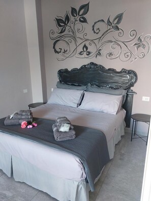 Een slaapkamer met een bed, kussens, een decoratief kunstwerk aan de muur, een nachtkastje en een klein tafeltje.