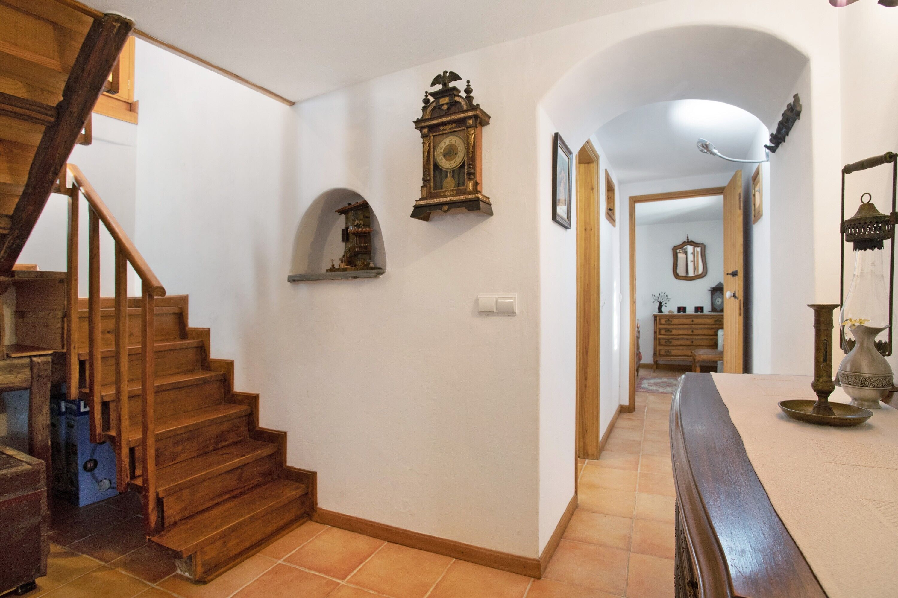 A staircase leading to a second floor, a wall-mounted clock, a mirror, and a dining area with a table and chairs.