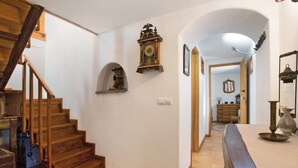 Un escalier menant à un deuxième étage, une horloge murale, un miroir et un coin repas avec une table et des chaises.