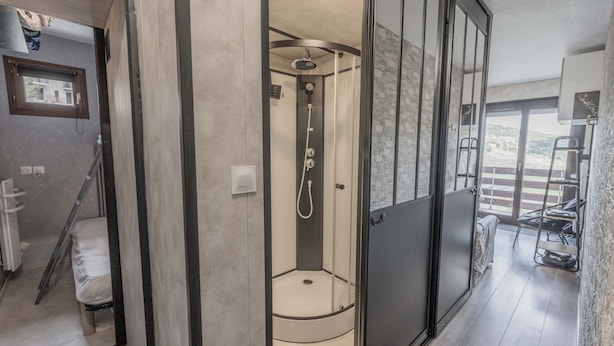Une salle de bain moderne dotée d’une douche à parois de verre, d’une fenêtre visible et d’un balcon aménagé avec du mobilier d’extérieur.