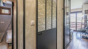 Un intérieur moderne avec un mur en pierre, une porte coulissante et une vue sur un balcon aménagé avec du mobilier d’extérieur.