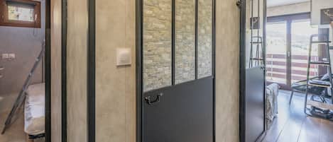 Un intérieur moderne avec un mur en pierre, une porte coulissante et une vue sur un balcon aménagé avec du mobilier d’extérieur.