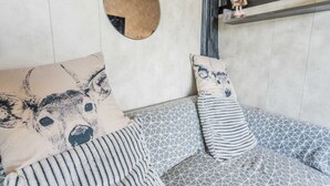 Une pièce chaleureuse avec un canapé à motifs, un miroir rond et une petite étagère sur laquelle est posé un ours en peluche.