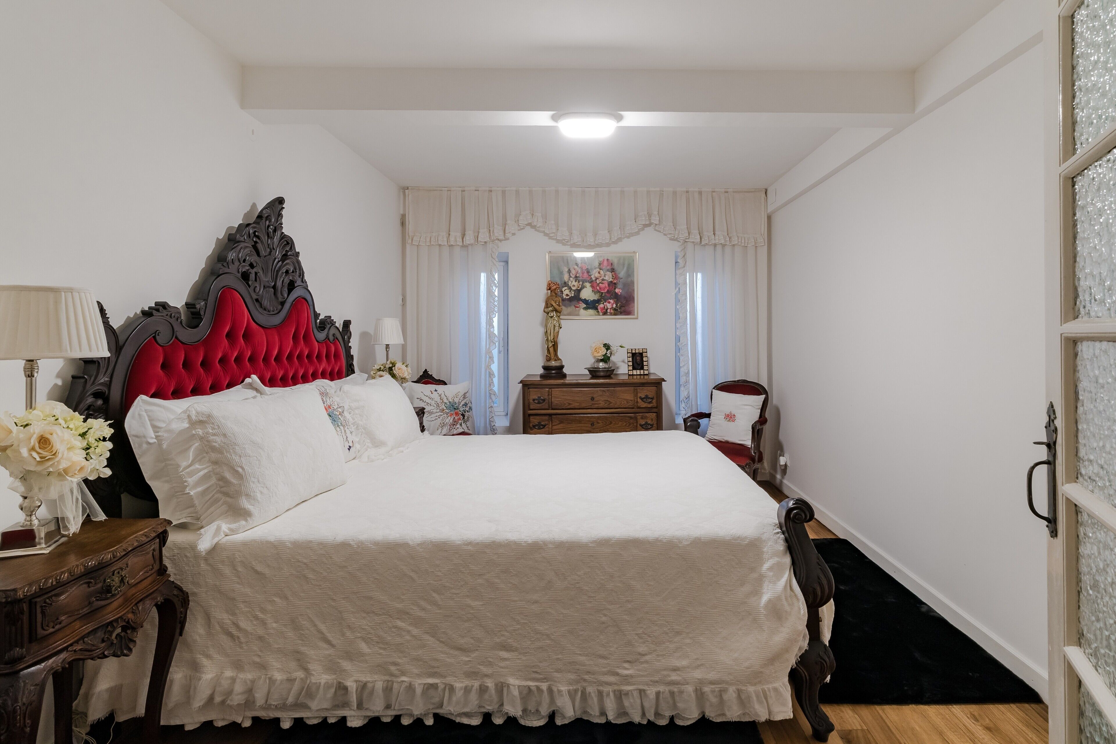 Une chambre à coucher avec un grand lit, une commode, une table de chevet et une fenêtre avec des rideaux.