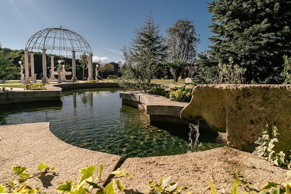 Un jardin avec un étang, un kiosque et une fontaine.