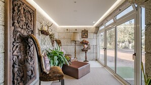 Een gang met een groot houten kunstwerk, een comfortabele bank, een potplant, een lamp en een uitzicht door grote glazen deuren.