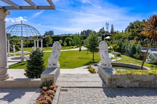 A garden with two stone lion statues, a pergola, and a dome structure in the background.
