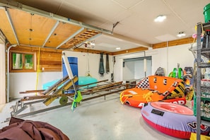 Un garage avec un plafond en bois, une piscine gonflable bleue, un radeau gonflable orange et un flotteur gonflable rouge.