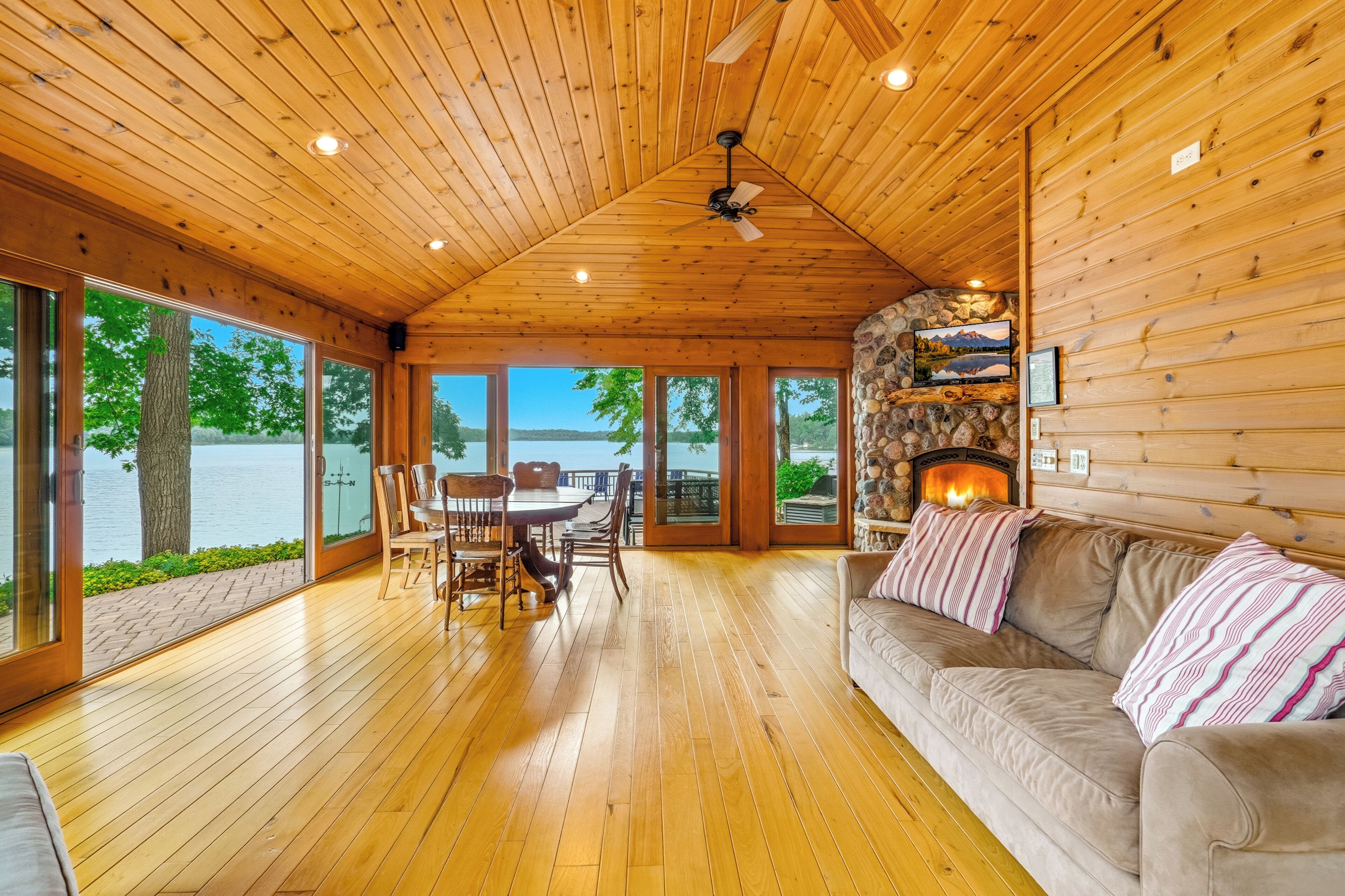 A wooden cabin interior with a dining area, a sofa, and a fireplace.