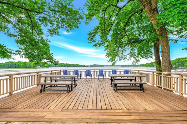 A wooden deck with picnic tables and chairs, overlooking a body of water. - Woodsy Waterfront Retreat on Gorgeous Balsam Lake (Balsam Lake)