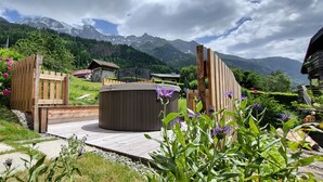 Een houten terras met een jacuzzi, omringd door weelderige begroeiing en een bergachtig landschap.