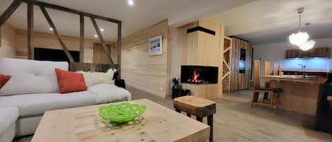 A modern living room with a sofa, a wooden coffee table, a fireplace, and a kitchen area.