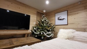 Een knus interieur met houten details, een flatscreen televisie, een kerstboom en een ingelijst schilderij aan de muur.