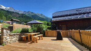 Een houten terras met picknicktafels en een stenen muur, met uitzicht op een bergachtig landschap.