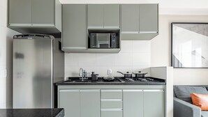 Una cocina moderna con gabinetes grises, un microondas integrado, un refrigerador de acero inoxidable y un sofá gris con un cojín naranja en el área de estar contigua.