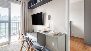 Una sala moderna con un ventanal grande, un televisor de pantalla plana, una mesa de comedor con sillas y un balcón con vista a la ciudad.