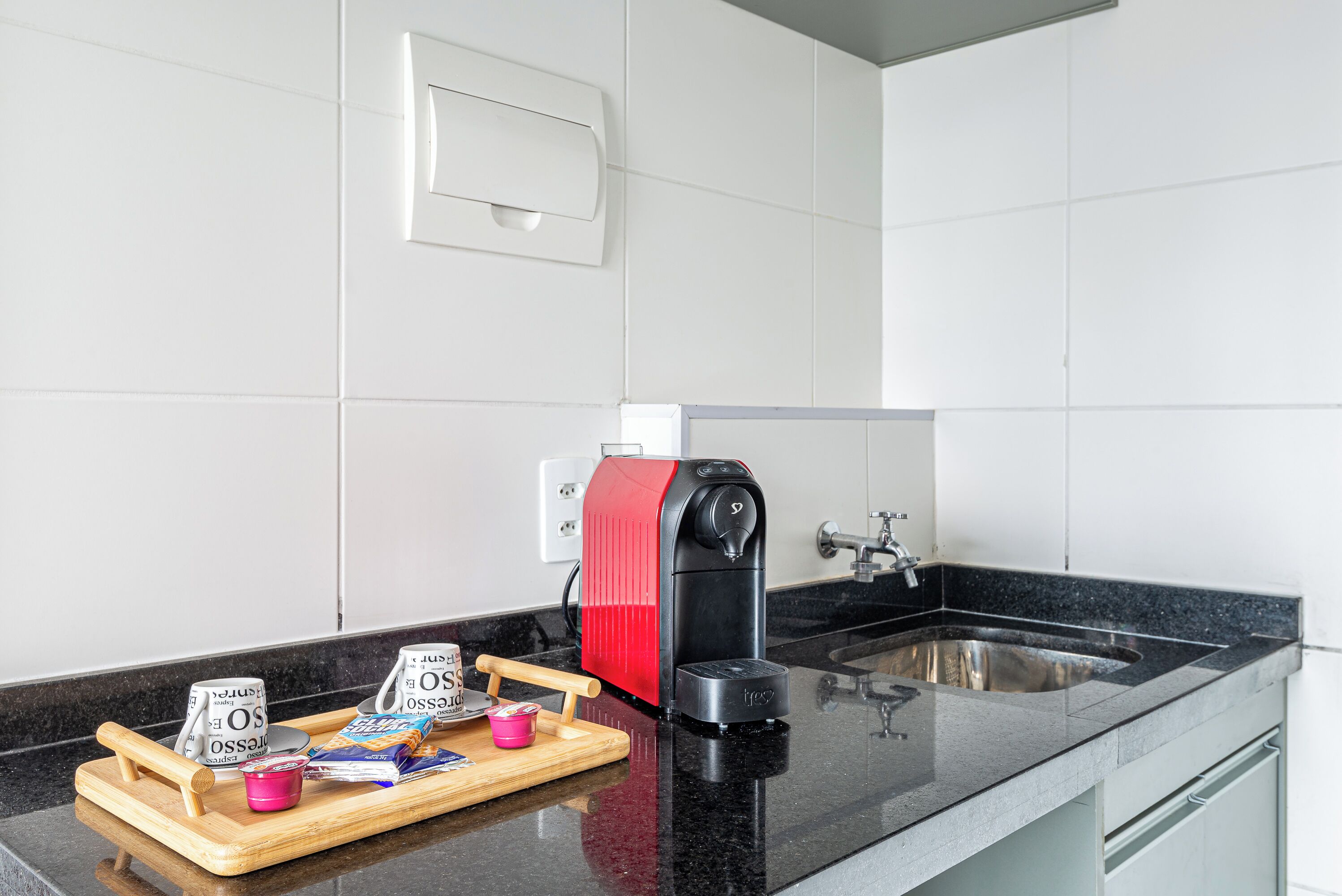 Una cucina con un piano di lavoro nero, una macchina da caffè, un lavandino e un vassoio con cibo.