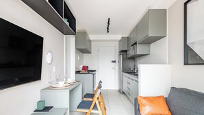 Una cocina moderna con armarios grises, un comedor con una mesa y sillas pequeñas, y un sofá gris con un cojín naranja.