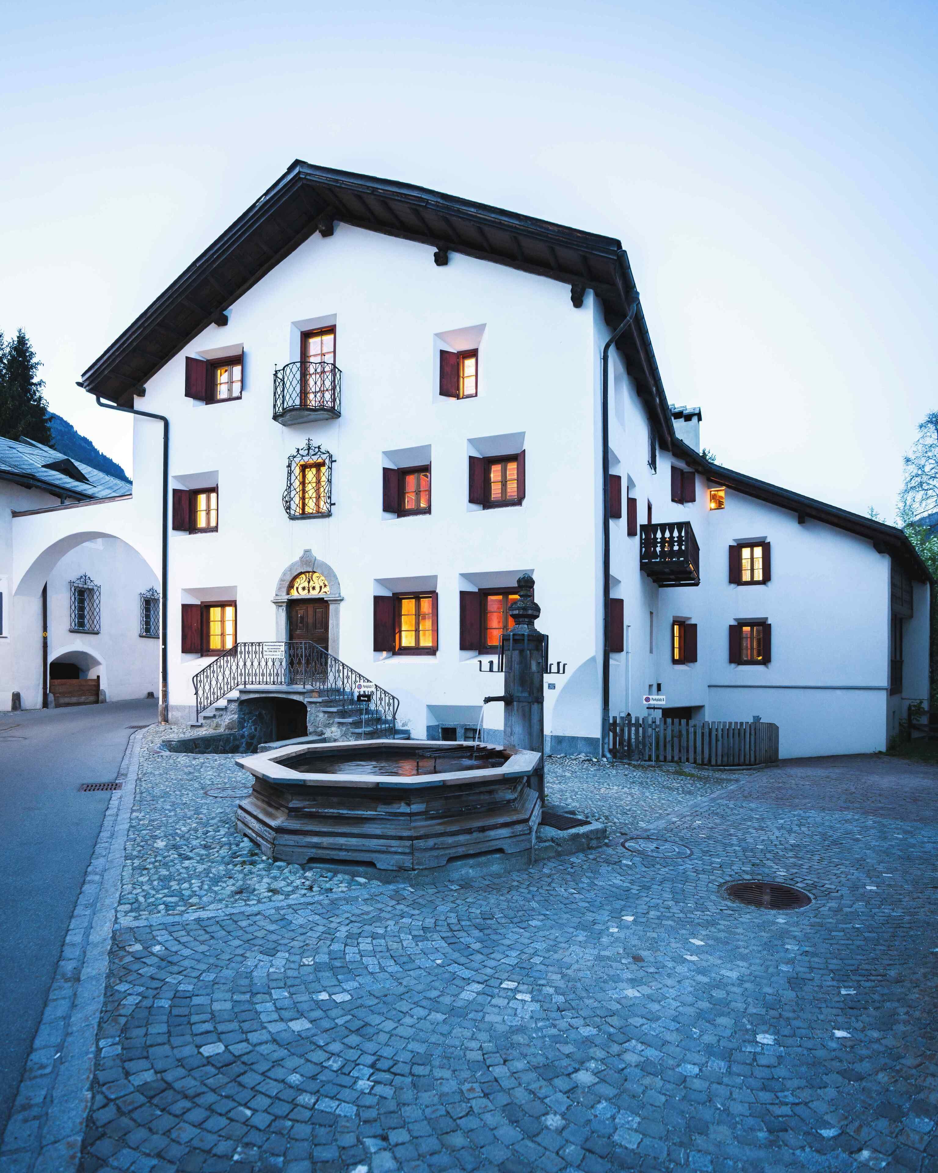 A traditional building with a stone staircase leading to a wooden door, a fountain, and a cobblestone courtyard.