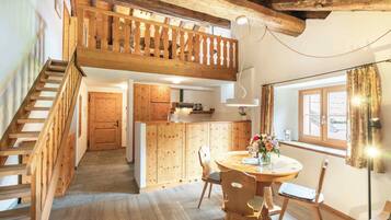 A wooden staircase leading to a loft bedroom with a balcony, a kitchen with wooden cabinets, and a dining area with a round table and chairs.