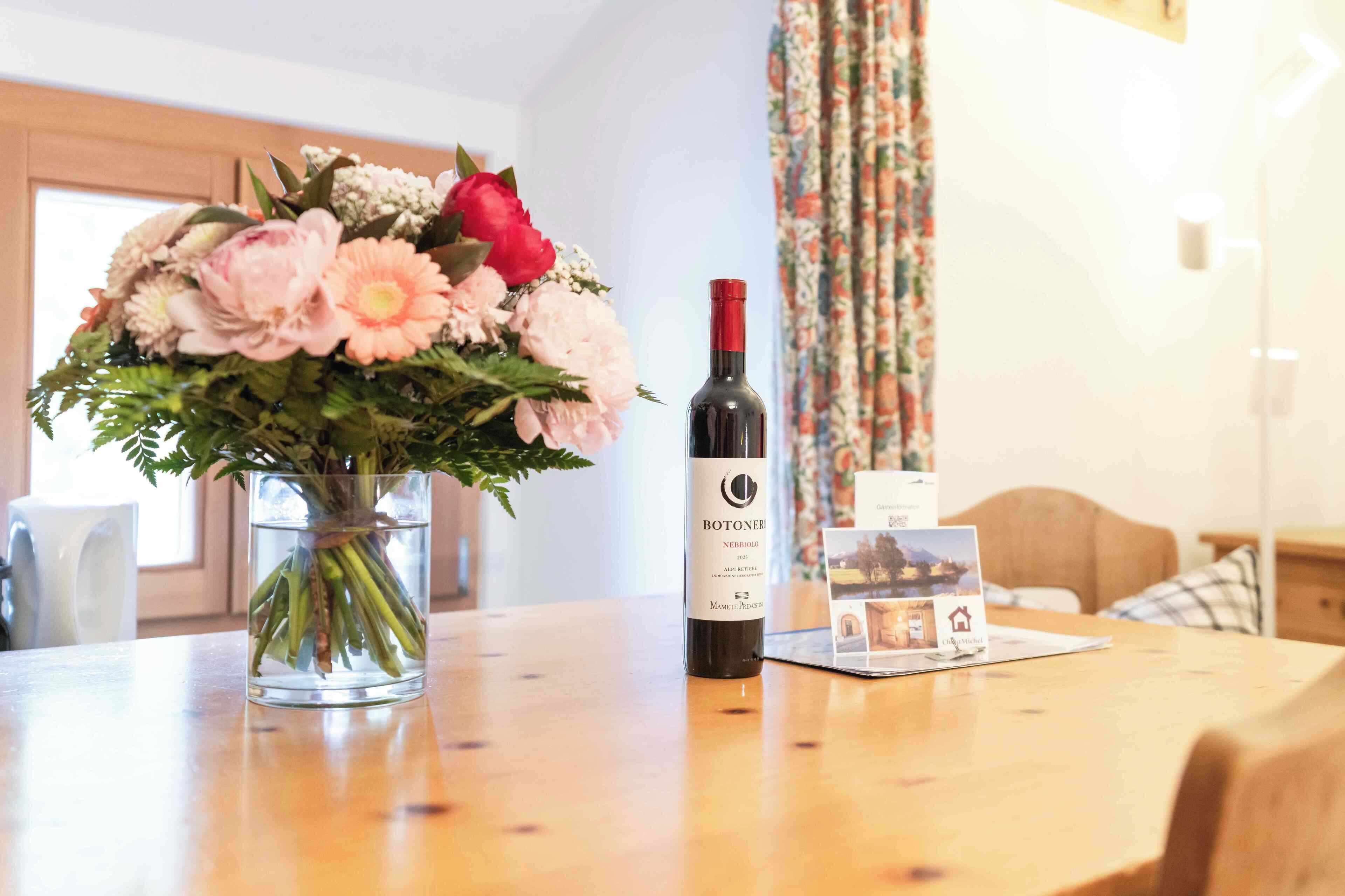 Een tafel met een fles wijn, een bloemenboeket en een brochure.
