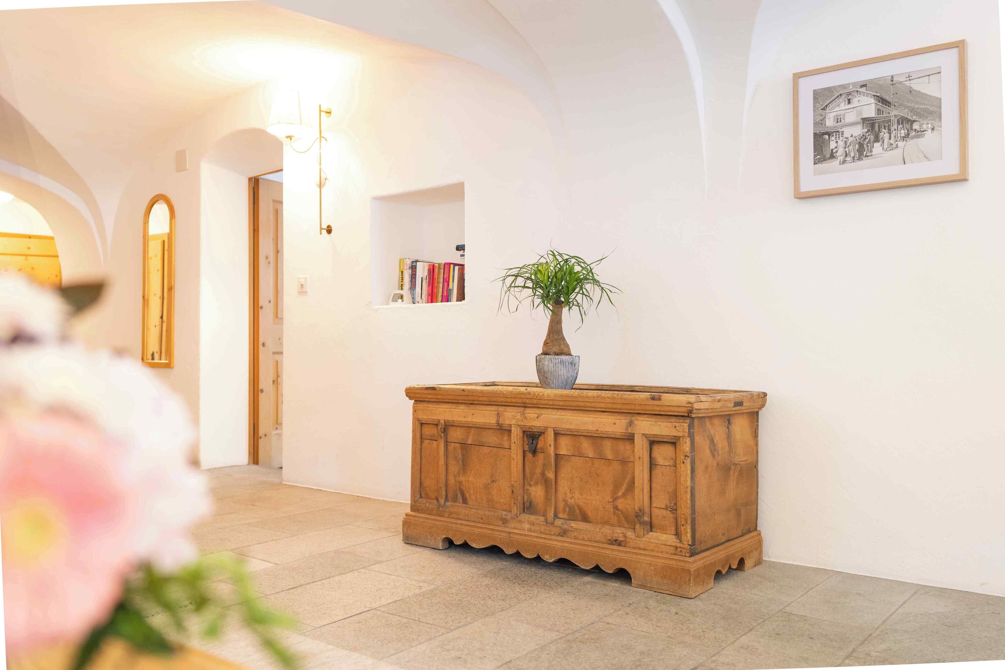 A hallway with a wooden console table, a potted plant, a framed photograph on the wall, and a bookshelf.