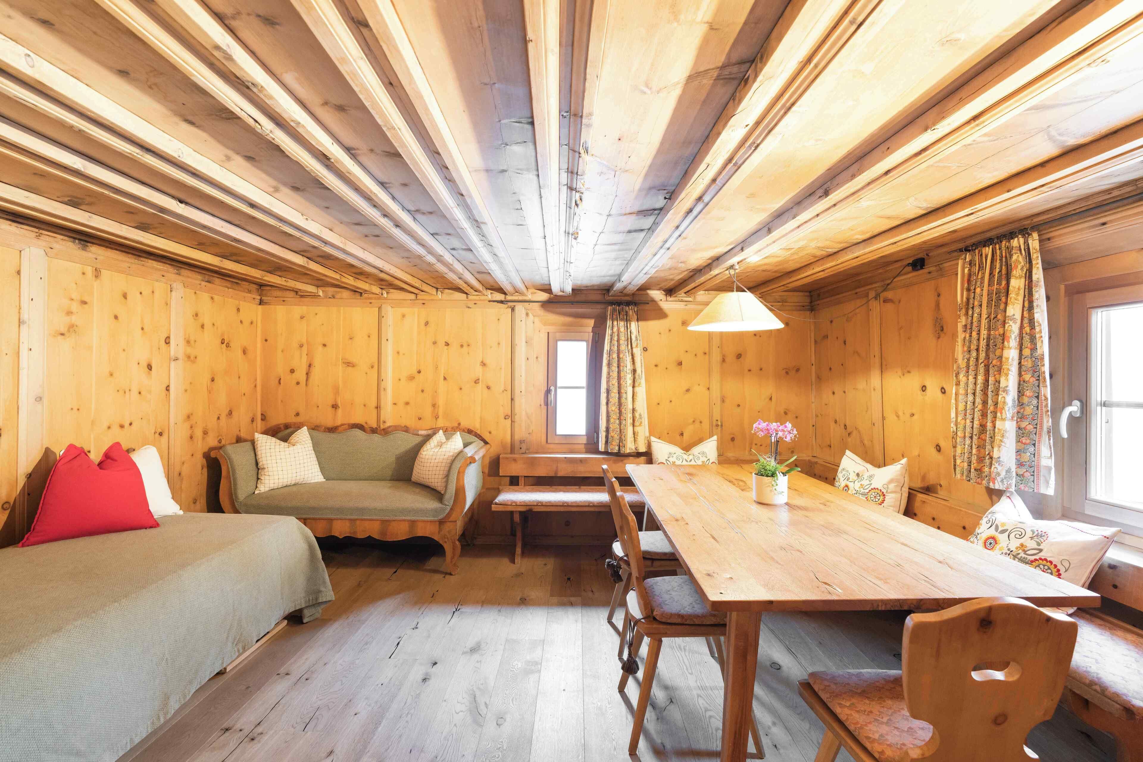 Interior de una cabaña de madera con una mesa de comedor, bancos, un sofá y una cama.