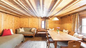 Interior de una cabaña de madera con una mesa de comedor, bancos, un sofá y una cama.