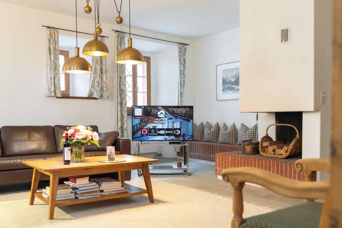 A living room with a brown leather sofa, a wooden coffee table with books, a TV on a stand, and a fireplace with a woven basket.