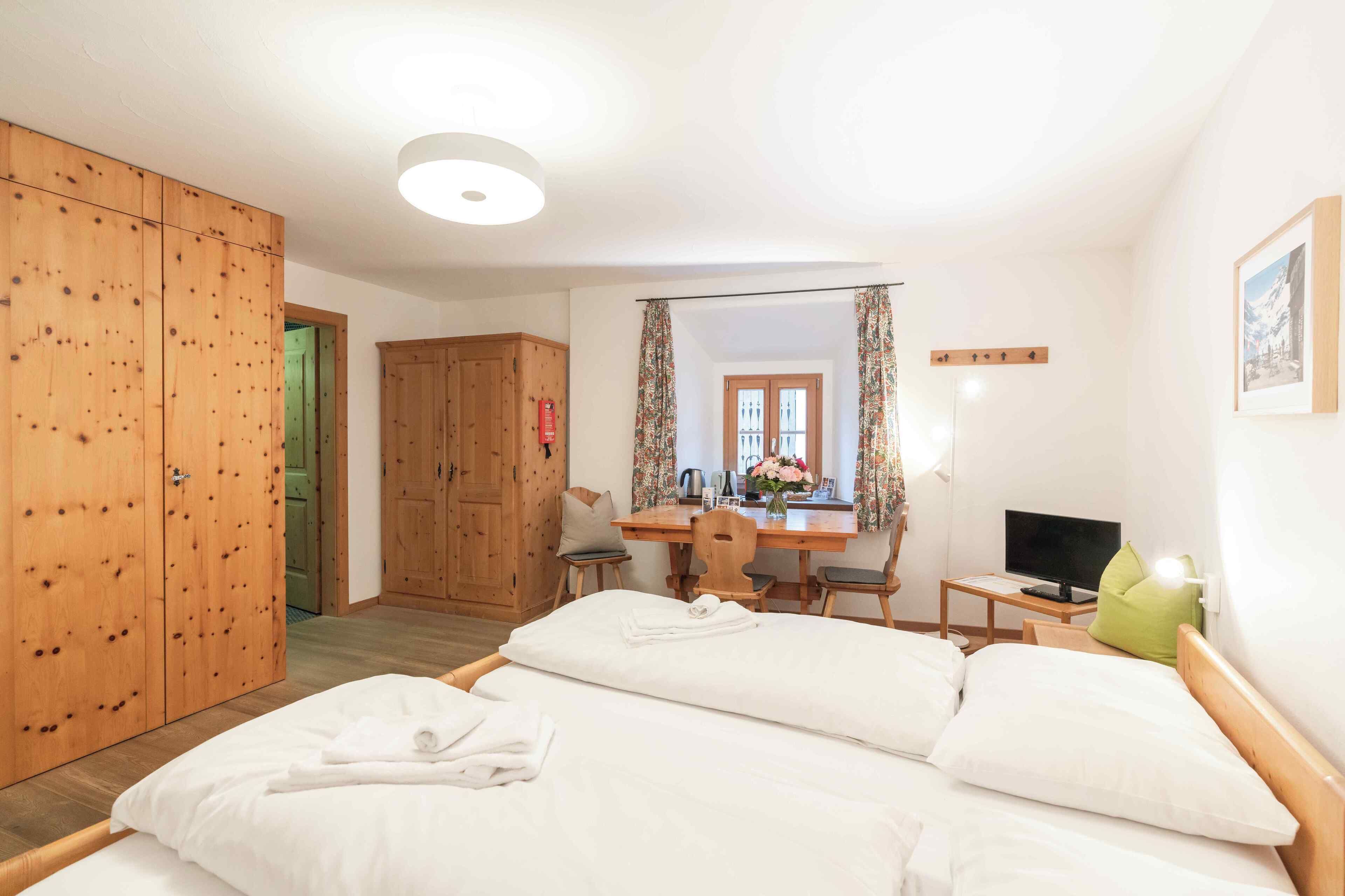 Ein Schlafzimmer mit zwei Betten, einem Holzschrank, einem Schreibtisch mit Stuhl, einem Fernseher und einem Fenster mit Vorhängen.