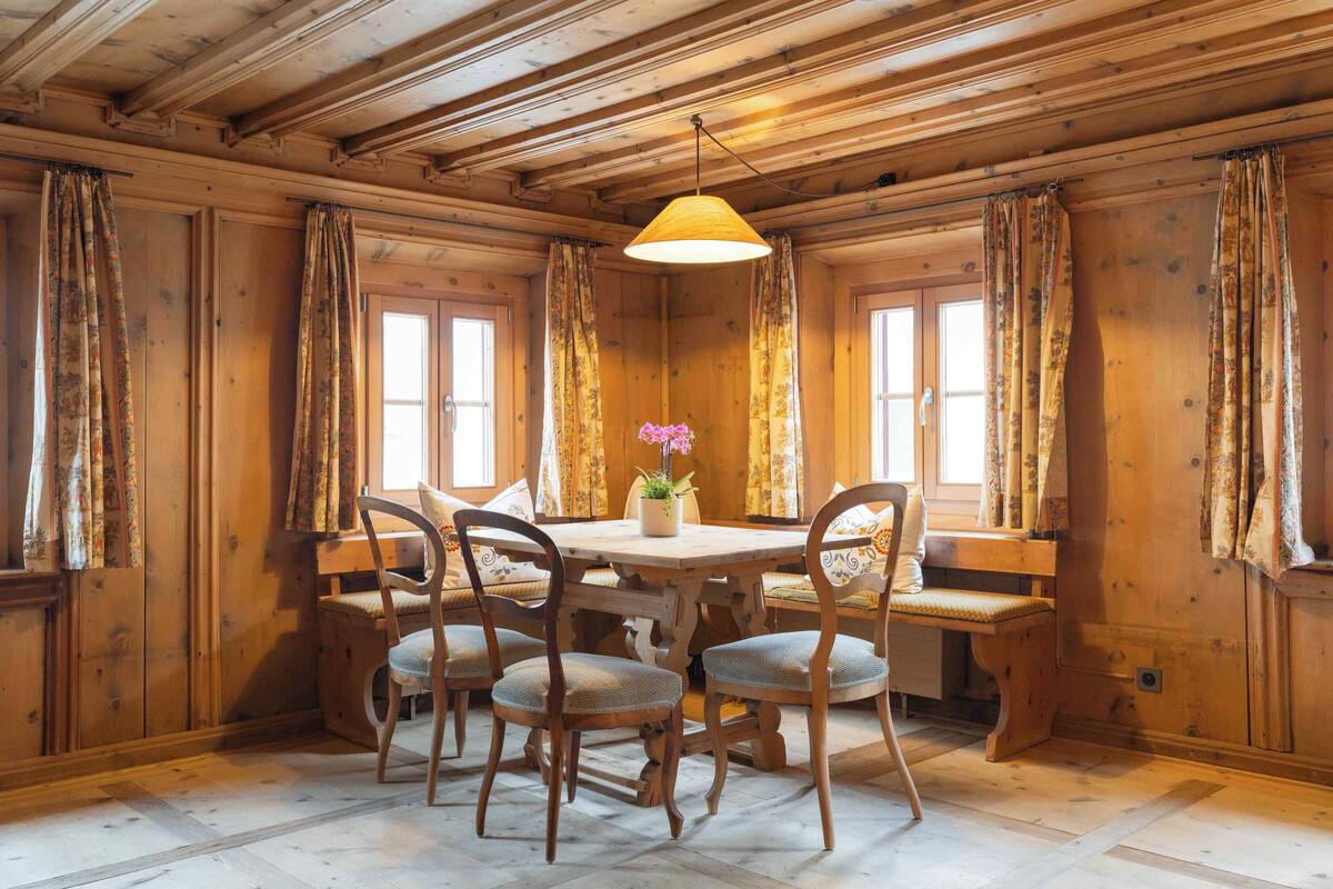 A wooden dining room with a round table, four chairs, and a bench.