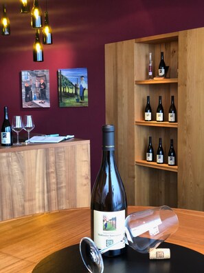 A wine tasting room with wooden shelves, wine bottles, and two paintings on the wall.