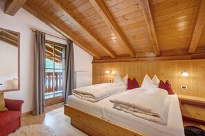 A wooden-paneled room with a bed, a nightstand, a red chair, and a window with curtains.