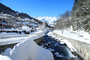 Une ville de montagne enneigée, avec une rivière, des bâtiments et un pont.