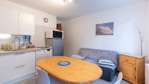 A compact kitchen with a microwave, sink, and cabinets, a dining table with chairs, a sofa, and a small wooden cabinet. - Cosy Stay in Barèges – Mountain Views, Wi-Fi, Free Parking, Near Ski Slopes (Barèges)