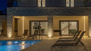 A modern outdoor pool area with lounge chairs and a stone-textured wall. - Amazing home in Nedescina (Nedescina)