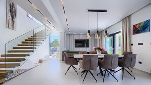 A modern dining area with a glass staircase, a flat-screen TV, and a dining table with chairs. - Amazing home in Nedescina (Nedescina)