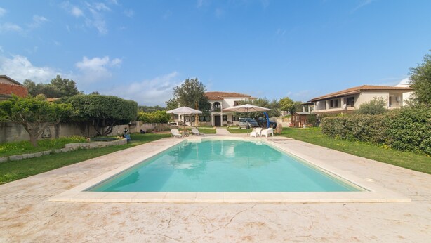 A swimming pool with lounge chairs, a covered patio, and a house in the background. - Room 'Perla' with Shared Pool, Wi-Fi and Air Conditioning (Torpè)