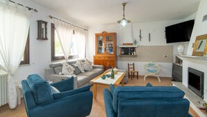 A living room with a sofa, chairs, a coffee table, a cabinet, a television, and a fireplace. - Room 'Perla' with Shared Pool, Wi-Fi and Air Conditioning (Torpè)