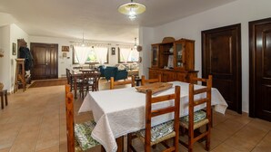 A dining area with a table set for four, wooden chairs, a cabinet, and a hanging light fixture. - Room 'Perla' with Shared Pool, Wi-Fi and Air Conditioning (Torpè)
