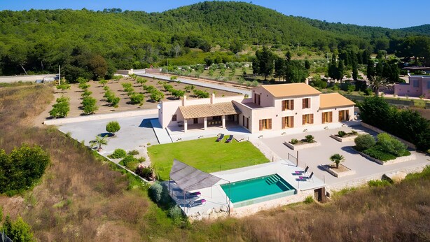 Eine Villa mit Swimmingpool, einer überdachten Terrasse und Blick auf einen grünen Hügel.