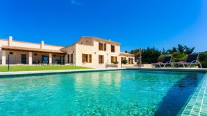 Ein Swimmingpool mit klarem Wasser, ein Gebäude mit einem Ziegeldach und Liegestühle.