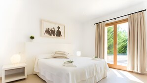 Ein Schlafzimmer mit einem Bett, einem Nachttisch, einer Nachttischlampe, einem gerahmten Bild und einem Fenster mit Vorhängen.