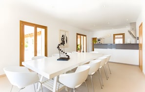 Een moderne eetruimte met een witte tafel en stoelen, een decoratief beeldhouwwerk en een keuken op de achtergrond.