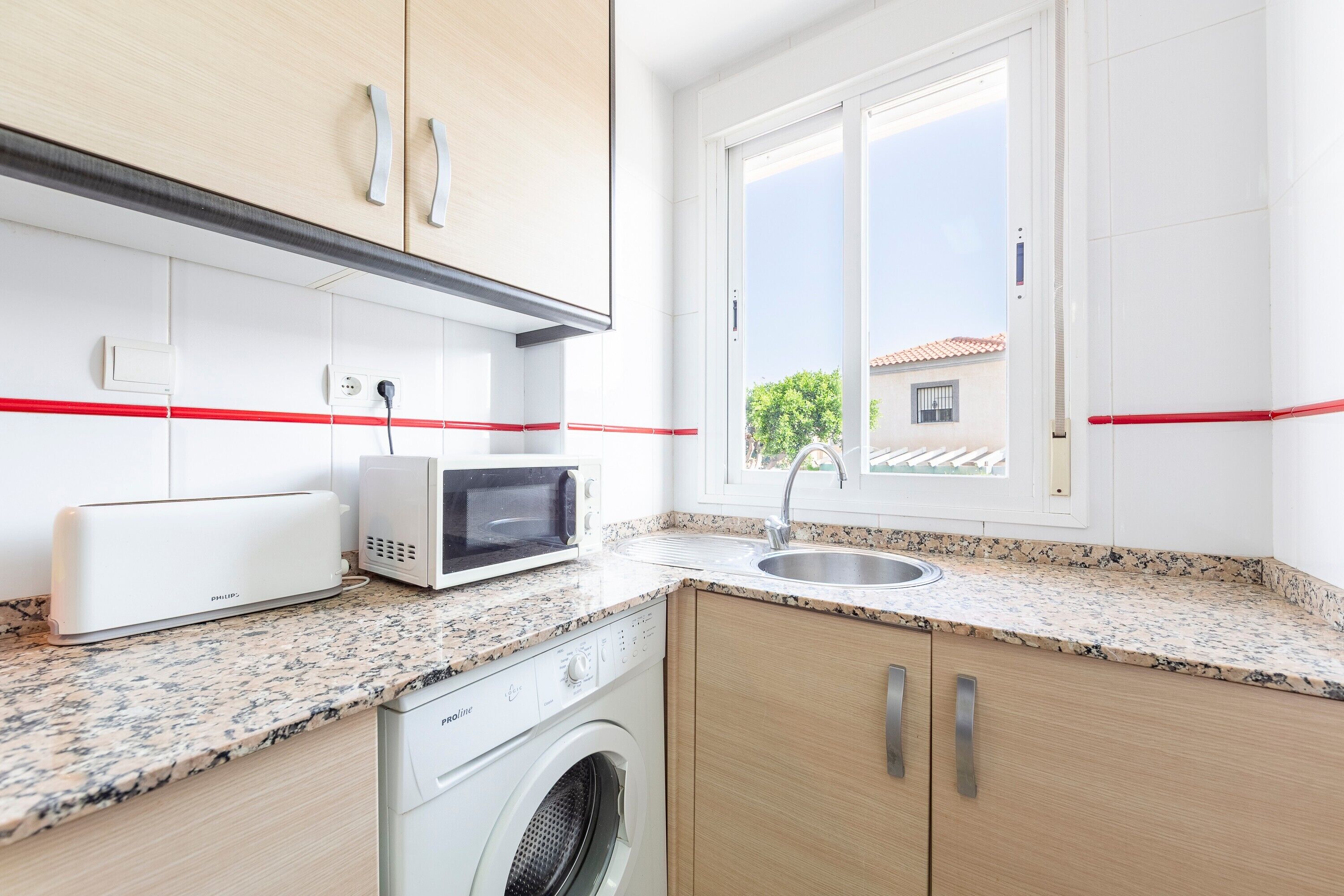 A modern kitchen with a washing machine, microwave, and a sink.