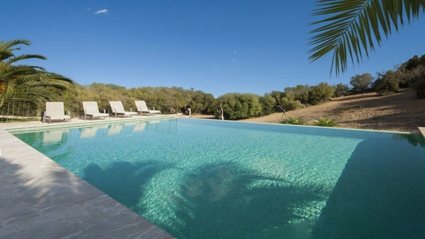 A clear swimming pool with lounge chairs, surrounded by trees and a clear sky.