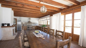 A spacious kitchen with wooden beams, a dining table with chairs, and a large window with curtains.